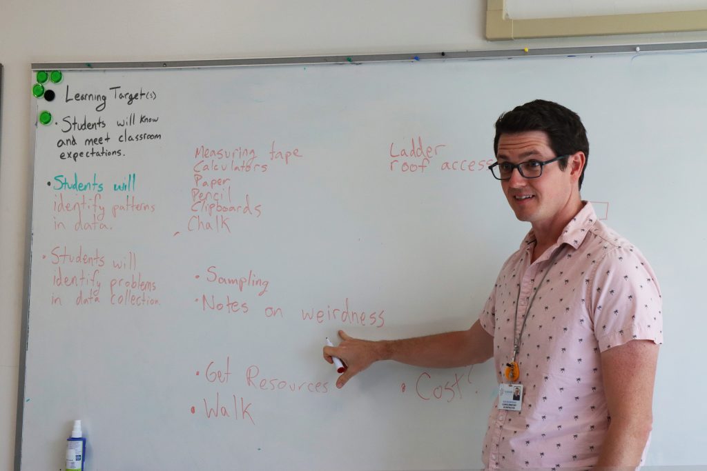 Photo of Sean Mournighan, Glenn's Academic and Intellectually Gifted (AIG) specialist, pointing to his whiteboard in class where the phrase 'notes on weirdness' is emphasized.  