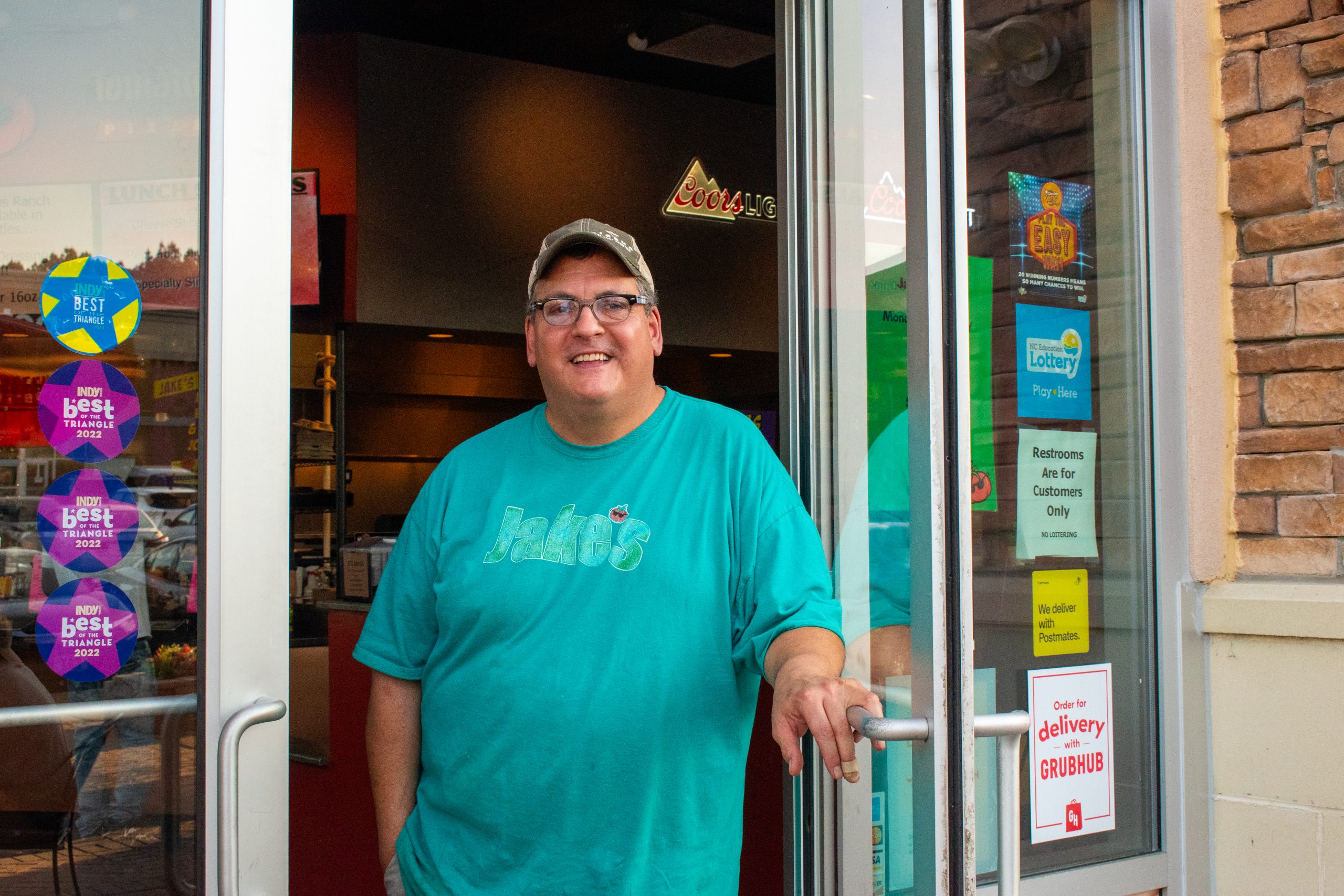 A photo of Glen Gordon, owner of Tomato Jake's Pizzeria, standing in the doorway of his restaurant in Durham, NC.