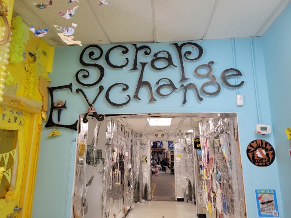 Sign reading "The Scrap Exchange" hanging above an open doorway on a blue wall